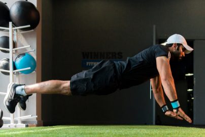 Middle Eastern man doing explosive pushups on gym turf.